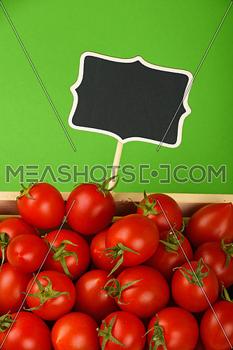 Fresh red ripe cherry tomatoes in small wooden box with black chalkboard price sign tag over green background, high angle view
