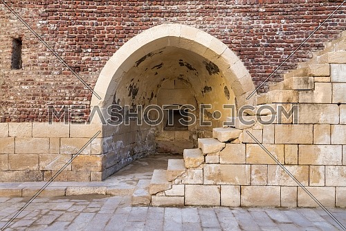 Exterior of ancient brick building with shabby stone stairway and crumbling arched alcove on street