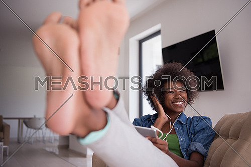 young beautiful African American woman enjoys listening to music with headphones and tablet in your armchair in her luxury home