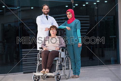 elderly sick woman in a wheelchair with medical staff in front of large modern hospital in the Middle East