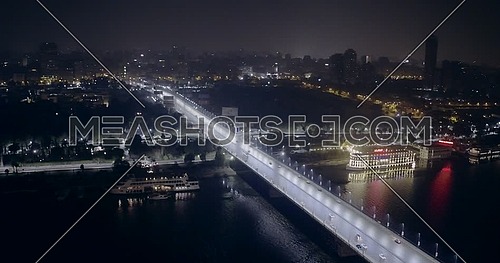 Aerial shot flying over the river Nile and 15 of May Bridge at night