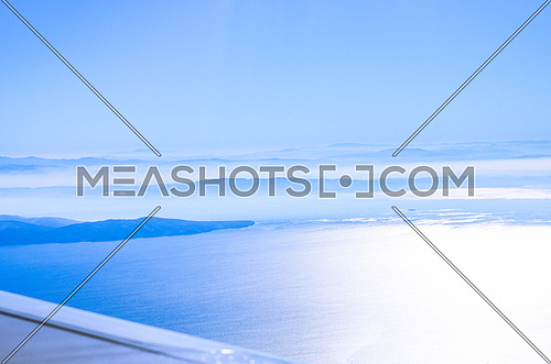 top view from a plane showing clear beautiful blue sky and the ocean underneath along side with an ending of a mountain