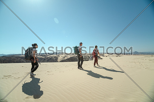 Long shot for group of tourists walking on sands with bedouin guide while exploring Sinai Trail from Ain Hodouda at day.