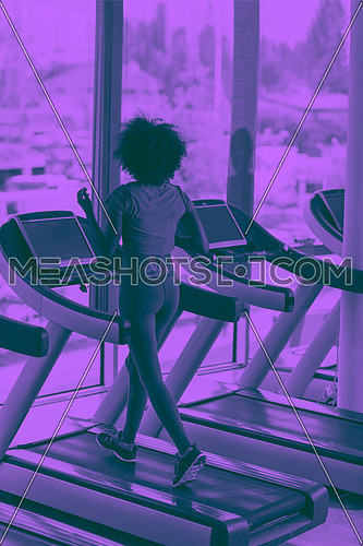 afro american woman running on a treadmill at the gym while listening music on earphones duo tone filter