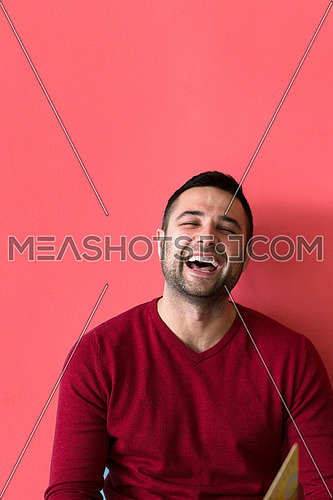 Young casual man sitting on floor and reading a book, isolated on red background
