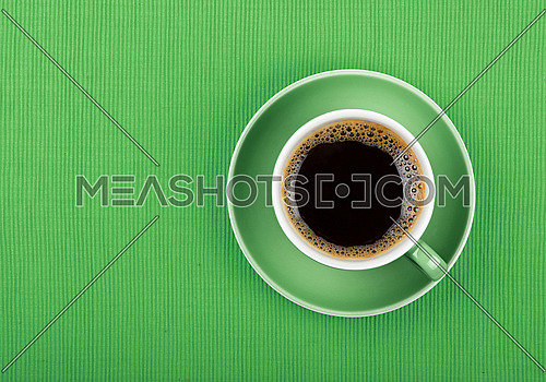 Full cup of black Americano or instant coffee on saucer over green tablecloth, close up, elevated top view