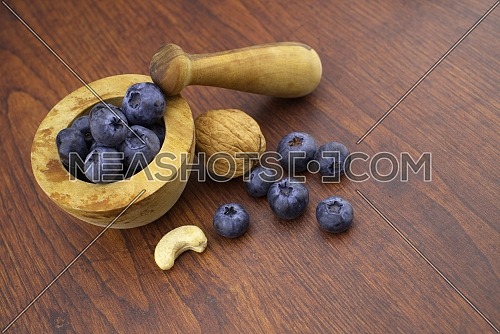 Wooden pestle and mortar with walnut, cashew nut and fresh blueberries on a wood table with copy space in a concept of a healthy diet and nutrition, high angle view