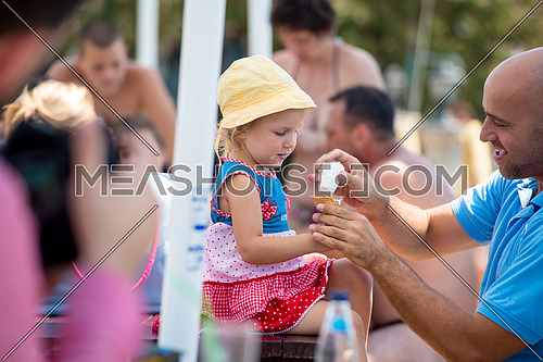 cute little girl having fun with her young father while eating ice cream by the sea during summer vacation holidays, celebration, children and people concept