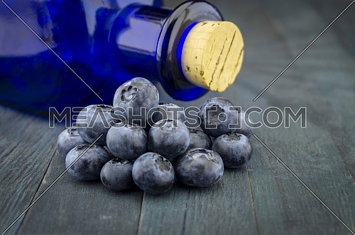 Fresh blueberries and corked blue glass pharmacy bottle on blue rustic board in close up
