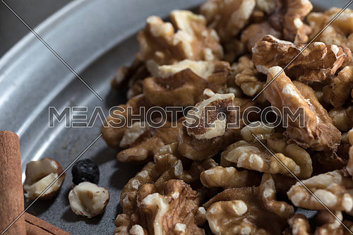 Walnuts in a metal tray with hazel nuts, raisin and cinnamon sticks