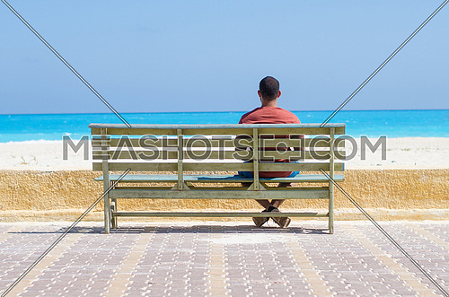 a lonely young man sitting on a bench by the sea