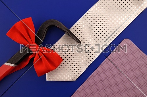 Still life with fashion accessories including an elegant necktie and red bow tie, crowbar and blank sheet of notepaper with copy space over a blue background