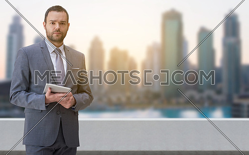 Portrait of young businessman standing on balcony in front of the big city
