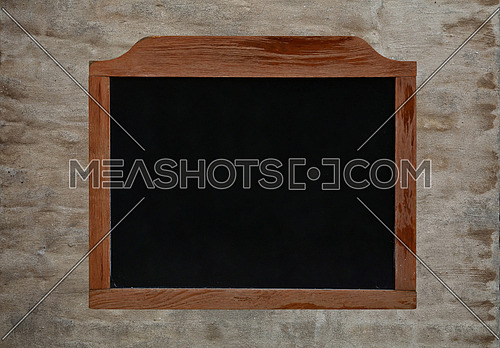 Old black school chalkboard blackboard sign in vintage brown wooden frame over background of grunge uneven gray daub plaster wall, close up