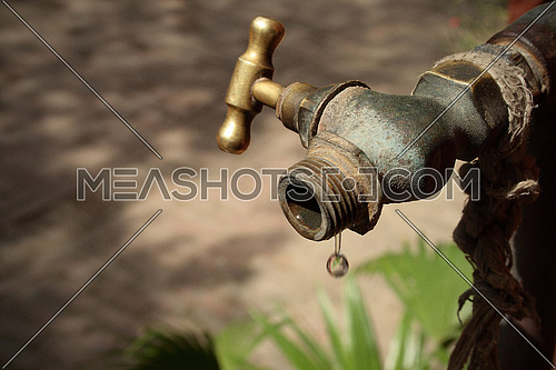 Image of a drop of water falling from an old metal conduct. The last drop of water