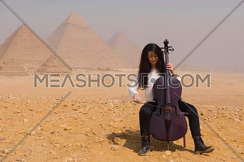 young famale chello player in egyptian desert with pyramids in background