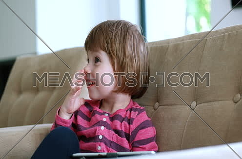 Cute little girl  sitting on coutch and using touchpad or tablet and smiling 