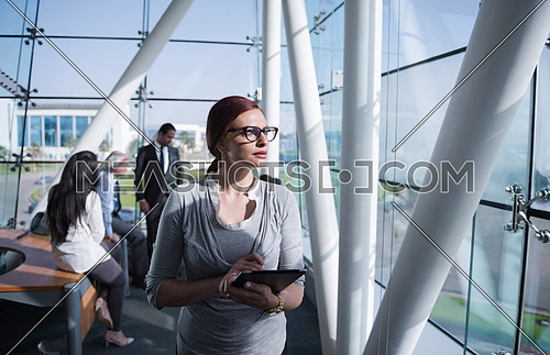 Portrait of a female executive wearing eye glasses and a group meeting is taking place at the background in a bright office
