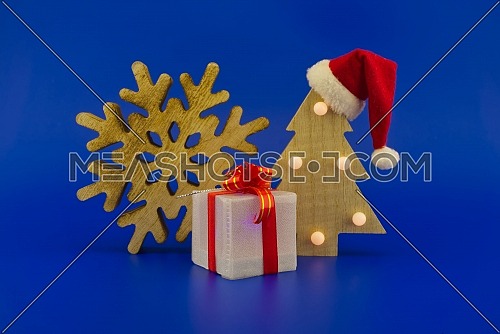 Snowflake decoration and Christmas tree with a Santa hat on top on a festive blue background. New Year and Christmas holiday season concept card decoration