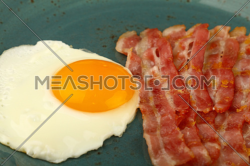 Close up English breakfast, sunny side egg and roasted bacon slices on blue plate, high angle view