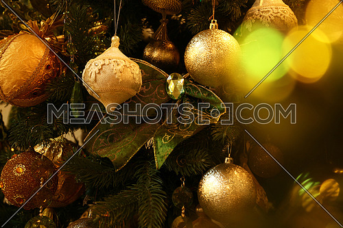 Close up handmade decorations hanging Christmas tree, bows, balls, spheres in warm light, front view