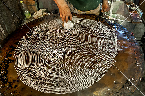 A man preparing kunafa the traditional way on a hot plate

 مظاهر شهر رمضان المبارك