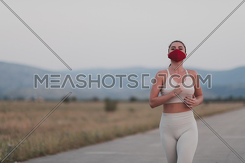 Determined fitness woman in short clothes wearing red protective face mask running outdoors in the city during coronavirus outbreak. Covid 19 and physical jogging activity, sport and fitness.
