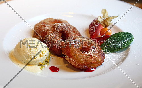 Close up portion of deep fried battered sweet apple rings with fresh ice cream and berries on white plate, traditional dessert of Bavarian German cuisine, high angle view