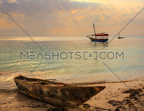 A beautiful beach with Traditional Fisherman's Dhow boat anchored at sunset with sunbeams.In the foreground old boat on the beach.Zanzibar coast,Tanzania.