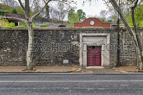 Closed old red wooden door, stone wall, and trees at Ciragan Street, Besiktas, Istanbul, Turkey