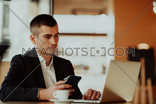 businessman sitting at the cafeteria with a laptop and smartphone. Businessman texting on smartphone while sitting in a pub restaurant. Businessman working and checking email on the computer.