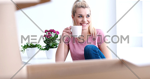 people, moving new place and repair concept   happy beautiful  young woman with many cardboard boxes sitting on floor with Cup at home
