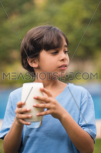 Middle Eastern boy enjoying with a glass of milk in his hand outside on summer day