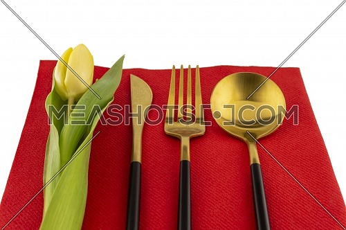 Gold cutlery and yellow tulip neatly displayed on a red place mat symbolic of a spring table setting and the season