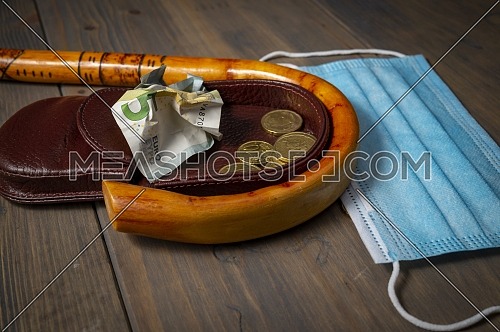 Conceptual Covid-19 flat lay still life with money spilling from an open purse onto a wooden table with cane and surgical mask alongside viewed from above