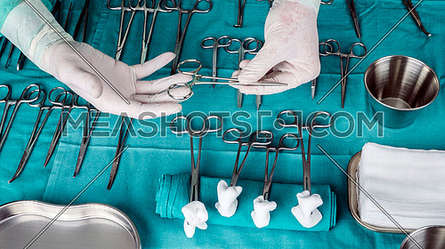 Surgeon working in operating room, hands with gloves holding scissors sutures, conceptual image, composicon horizontal