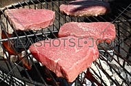 Raw beef bbq steaks cooking roasting on outdoors flame barbecue grill, one being put on fire and poured dredged with salt, close up