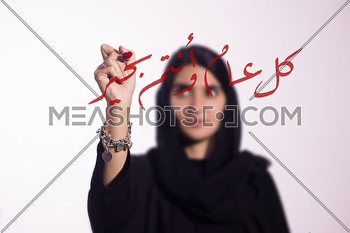 Arabian middle eastern business woman writing with a marker on virtual screen in arabic كل عام و انتم بخير suggesting season greeting "happy new year" "Happy Birthday"
isolated on white background