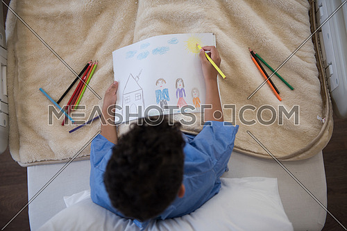 top view of little middle eastern boyl painting home and family at hospital bed