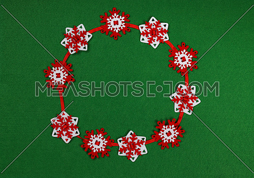Close up circle of red and white snowflake shaped Christmas decoration garland over green felt background with copy space, table top view, flat lay