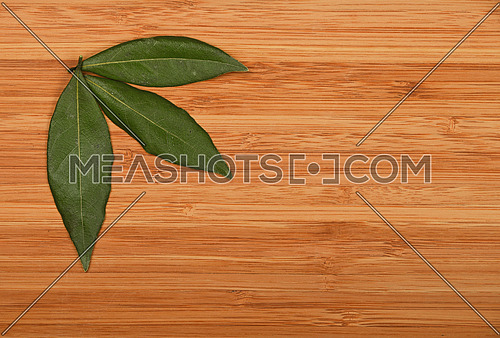 Group of three bay laurel leaves in corner of bamboo wooden chopping board background