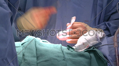 Closeup of surgeon's hands Cleaning incision with a rag while stitching