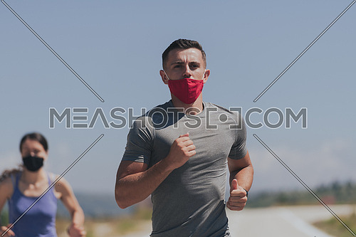 Young man and woman in protective masks running and doing exercises outdoors in the morning. Sport Active life Jogging during quarantine. Covid-19 new normal. Selective focus.