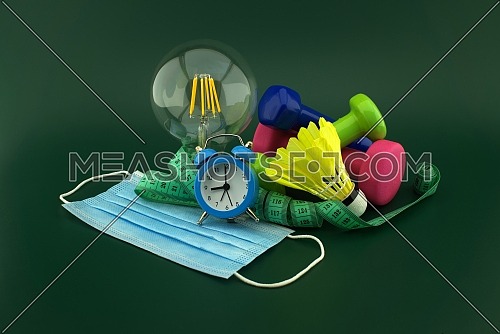 Starting healthy lifestyle after quarantine idea concept with medical face mask, lamp light bulb and various sports inventory including dumbbells weights, shuttlecock and measuring tape