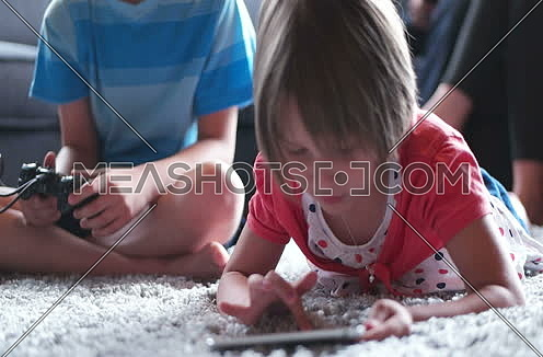brother palying video games while sister using tablet in living room