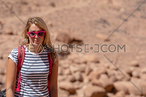 Long shot for a female tourist wearing a pink glasses and travel backpack taking exploring at Sinai Mountain for wadi Freij at day.