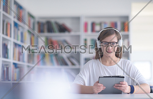 female student study in school library, using tablet and searching for informationâs on internet. Listening music and lessons on white headphones
