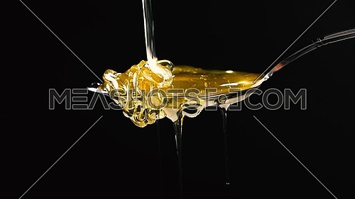 Close up fresh thick fluid acacia honey pouring and flowing from metal spoon over black background with copy space, low angle side view, slow motion