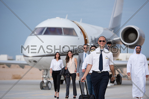 Young middle eastern successful pilot walking with clients in front of private airplane