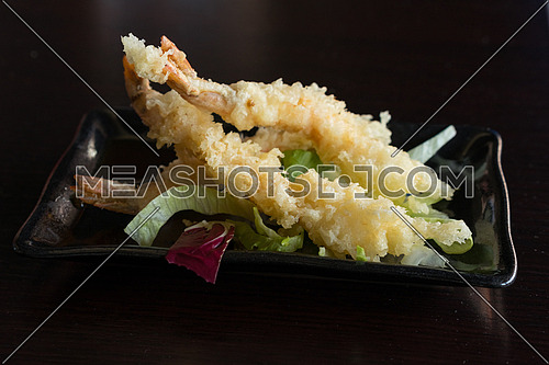 Japanese Cuisine - Tempura Shrimps (Deep Fried Shrimps) with sauce and vegetables on a black plate. Black background,shallow depth of field.